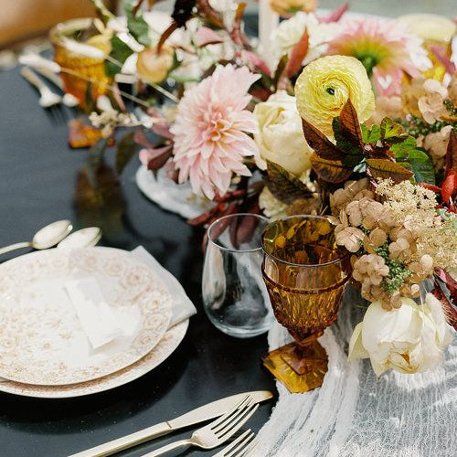 Decorative table setting with flowers, plates, and cutlery on a dark surface.